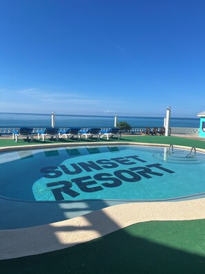 A clear blue sky, a pool with 'Sunset Resort' written on it, and a view of the ocean. - Beyond Sunset Resort & Villas (Treasure Beach)
