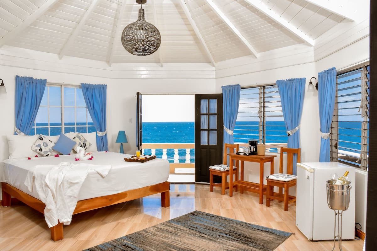 A bedroom with a bed, a desk, a chair, and a view of the sea.