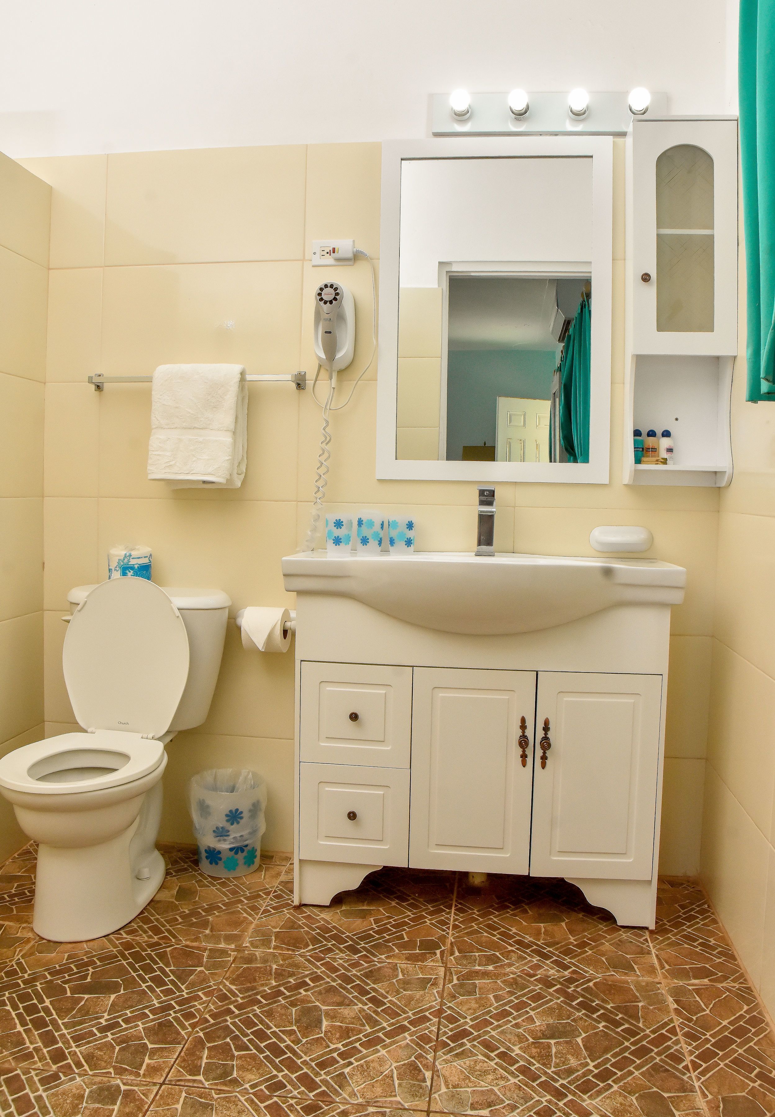 A bathroom with a toilet, sink, vanity, and a mirror with lights above.