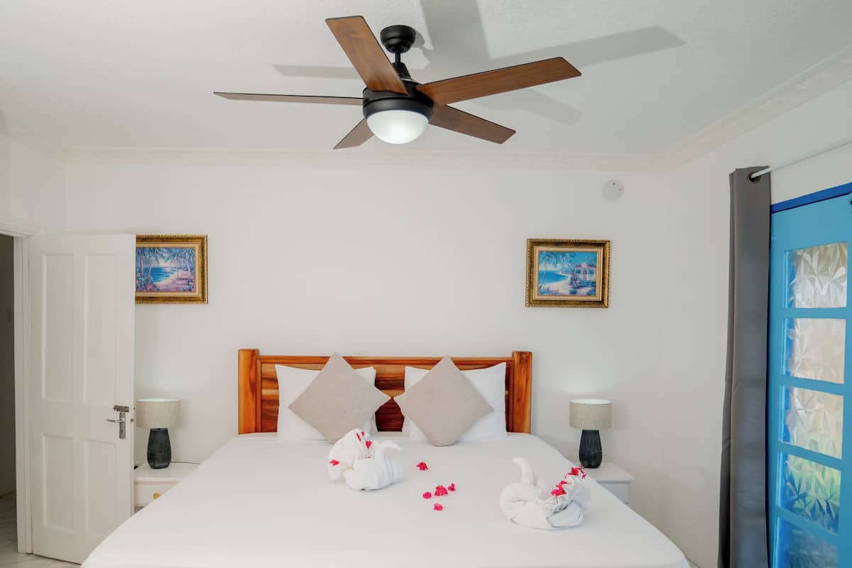 A hotel room with a bed, a ceiling fan, two wall-mounted paintings, and a blue curtain.