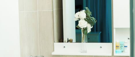 A bathroom with a white sink, a mirror above it, and a vase with flowers.