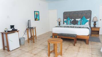 A bedroom with a bed, bedside tables, a desk, a refrigerator, and a trash bin.