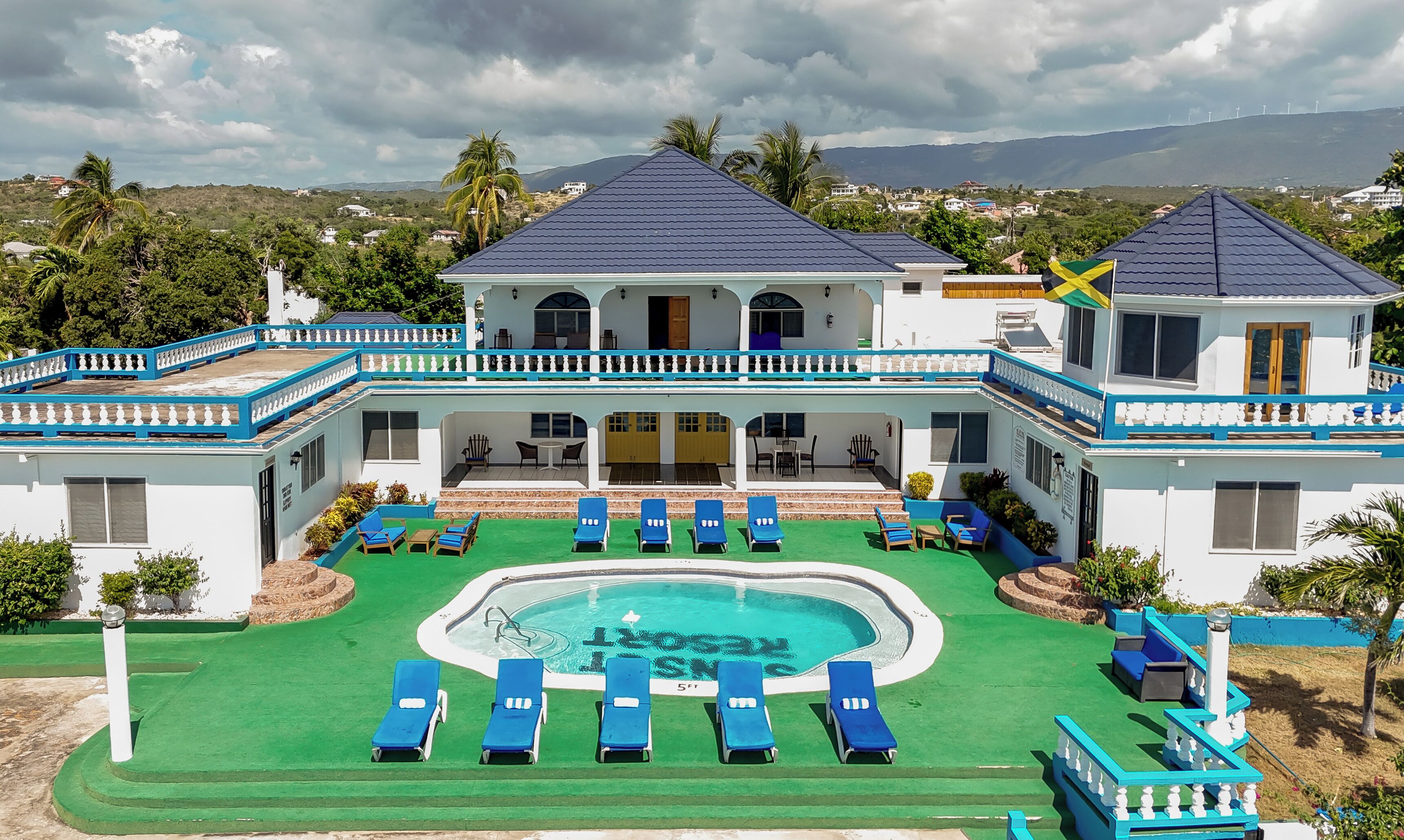 Ein zweistöckiges Gebäude mit Swimmingpool, mehreren Liegestühlen und Blick auf die umliegende Landschaft.