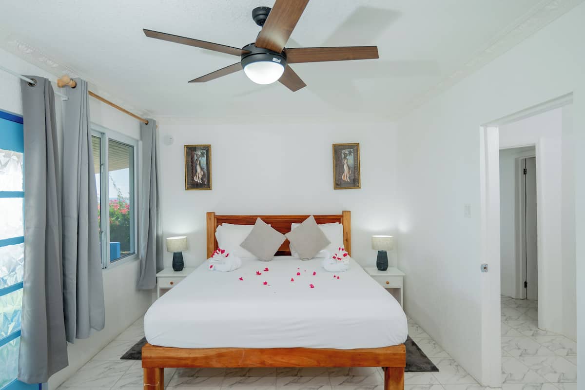 A bedroom with a wooden bed, a ceiling fan, two bedside lamps, and a window with curtains.