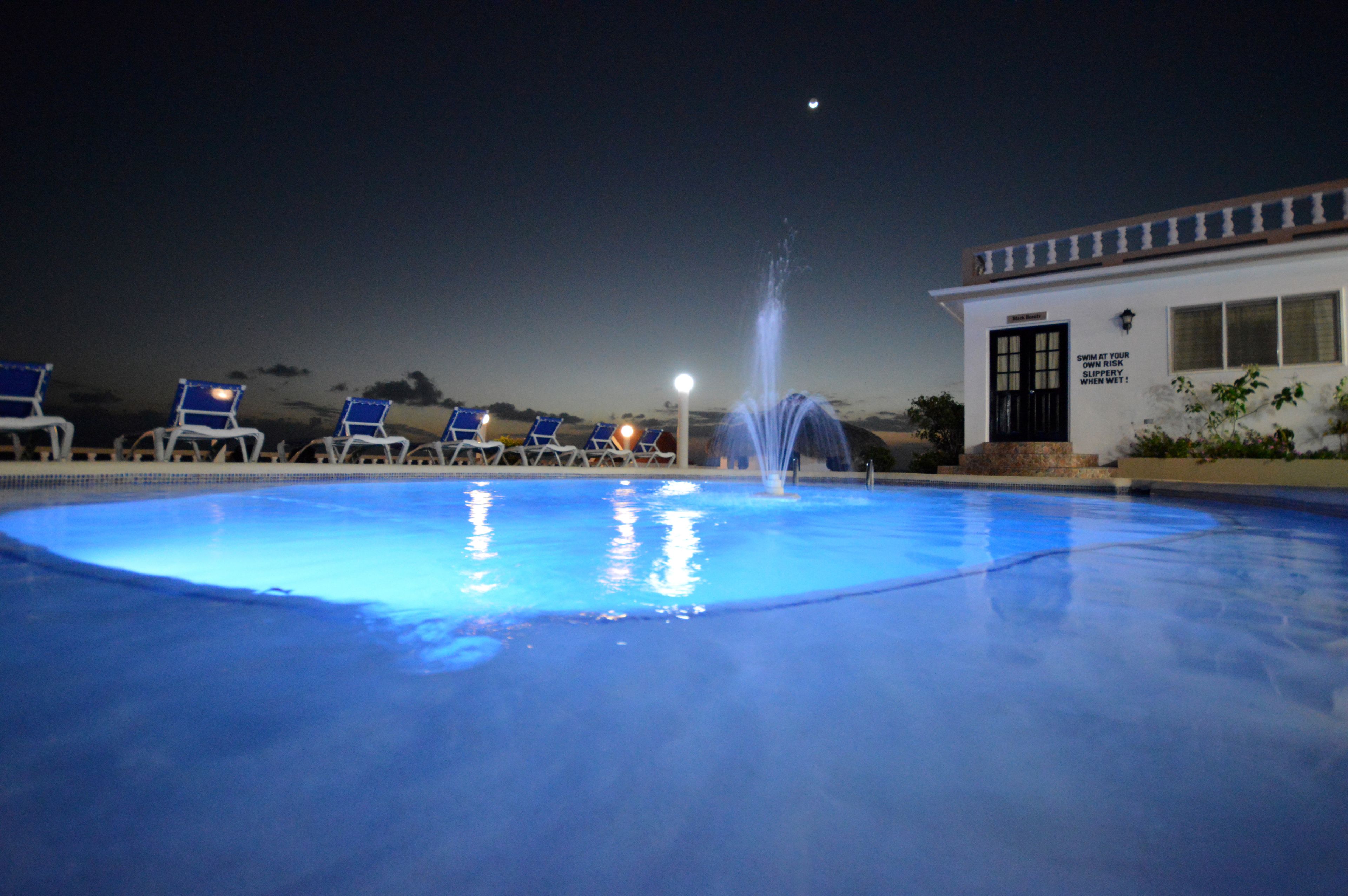 A swimming pool with a fountain, surrounded by lounge chairs and a building with a sign.