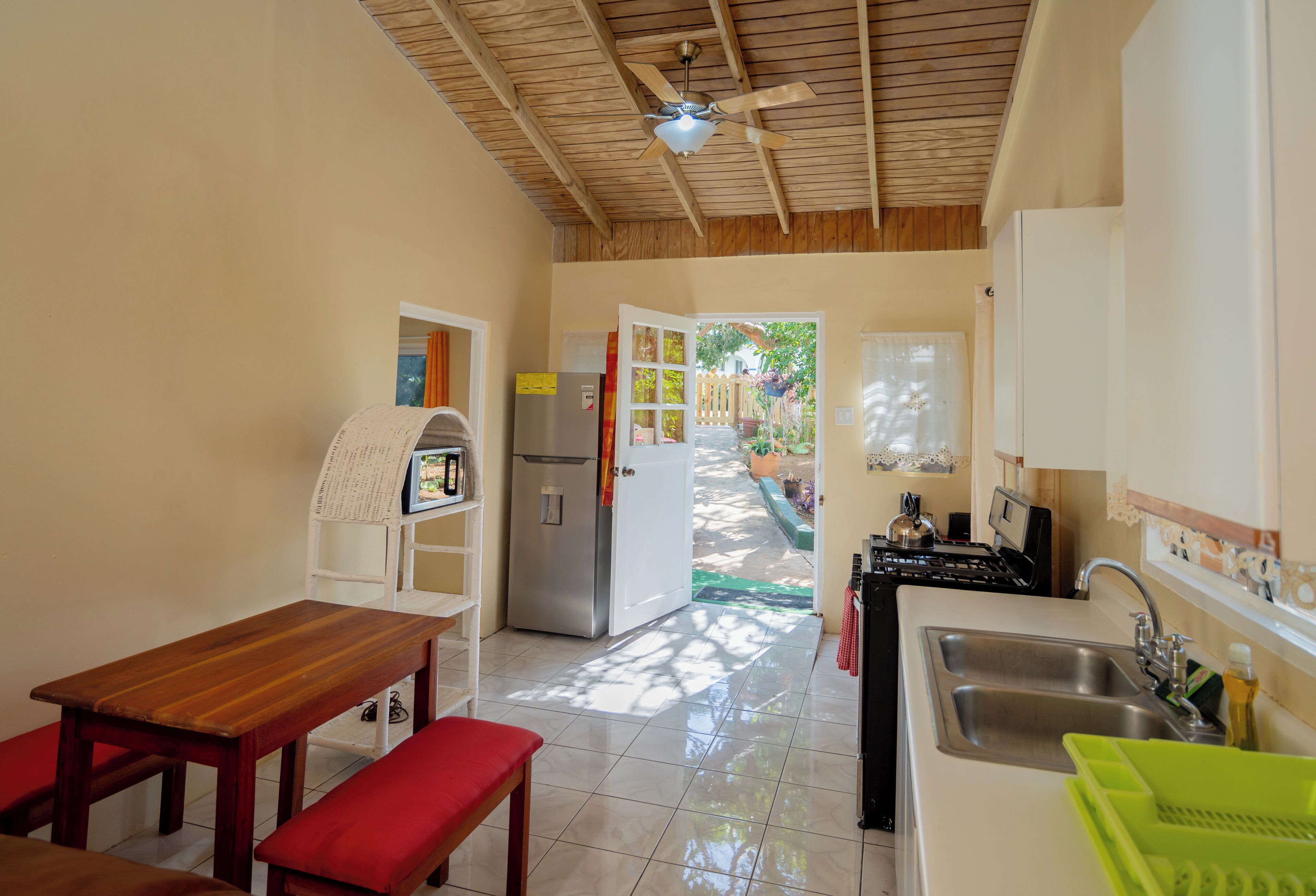 A compact kitchen with a wooden ceiling, a refrigerator, a stove, and a sink.