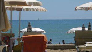 A beach with umbrellas and lounge chairs, a clear view of the sea, and a distant sailboat. - Residence Florida (Caorle)