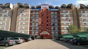 A multi-story hotel with a central entrance, balconies on each floor, and a parking area in front. - Residence Florida (Caorle)