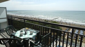 A balcony with a table and chairs overlooking a beach with umbrellas and people. - Residence Florida (Caorle)