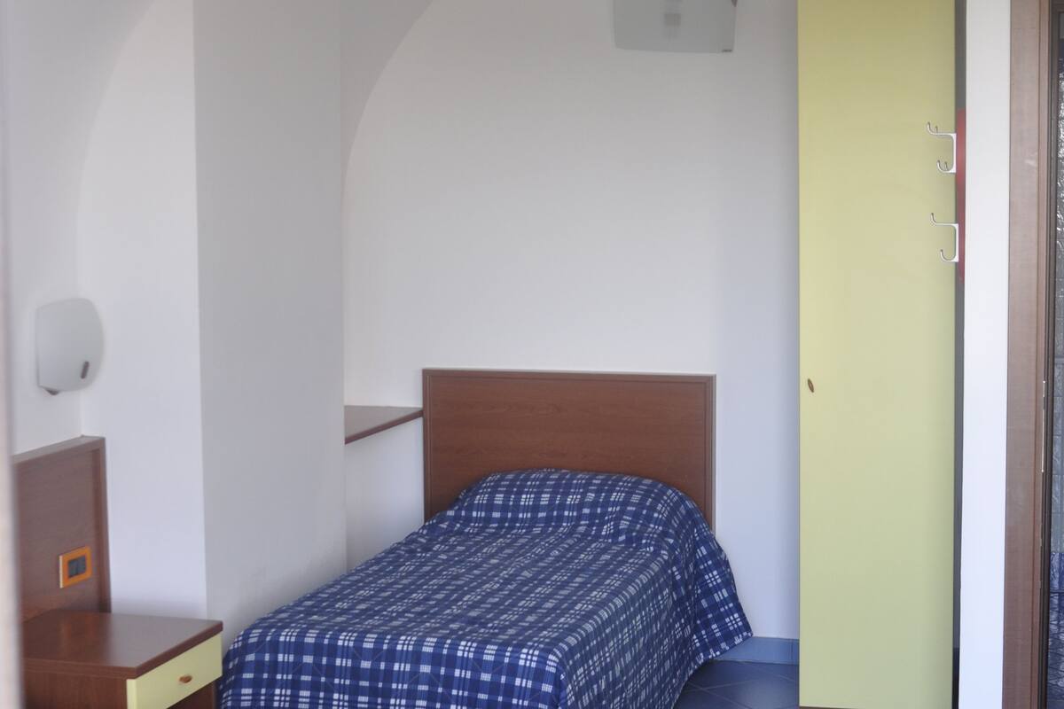 Una habitación con dos camas, un cabecero de madera, una mesita de noche pequeña, una lámpara de pared y una puerta con un panel amarillo.