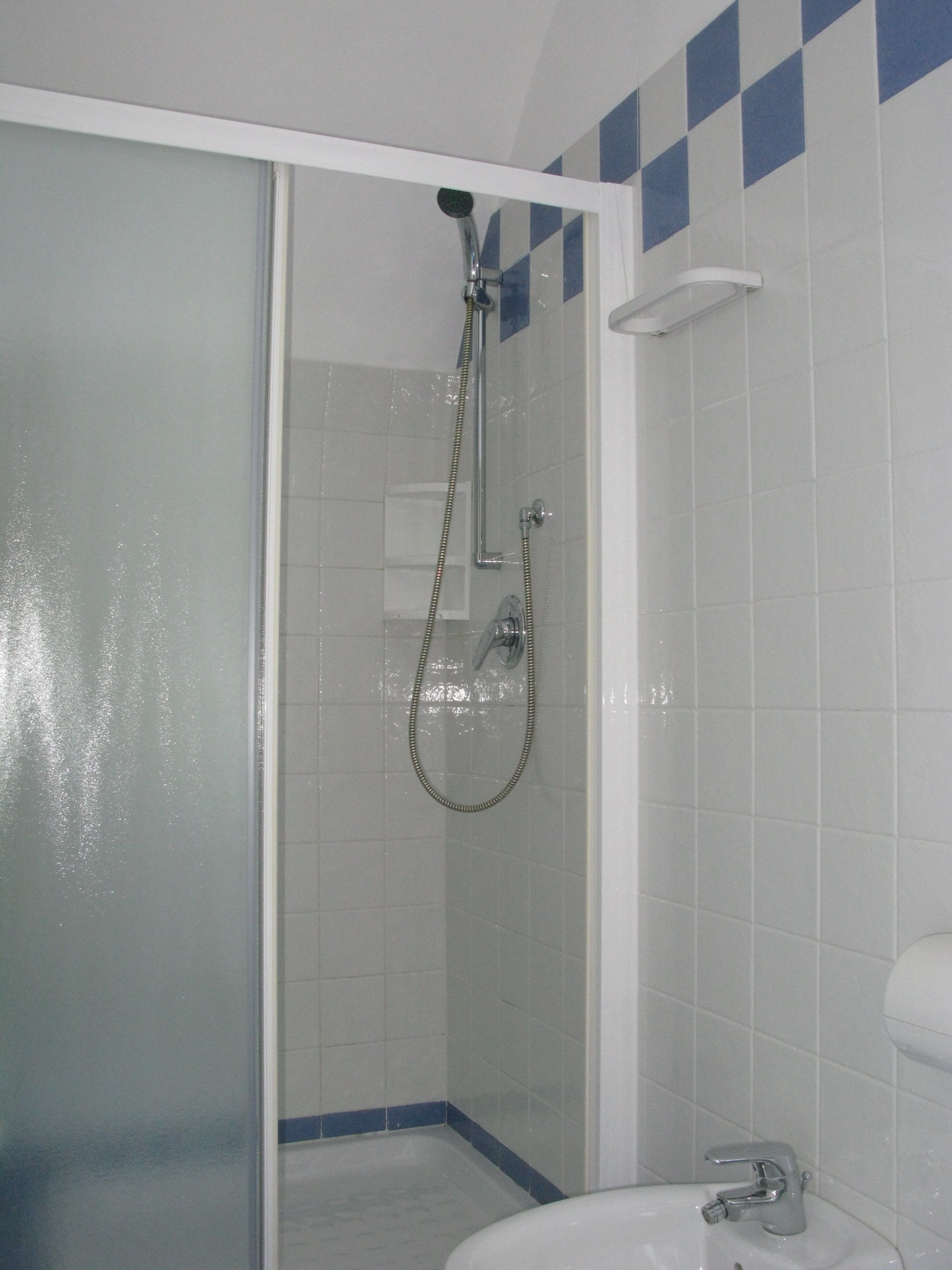 A bathroom with a glass shower enclosure, a white sink, and blue-tiled walls.