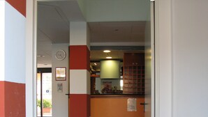 A hallway with a red and white striped wall, a clock, and a counter with a menu board. - Residence Florida (Caorle)