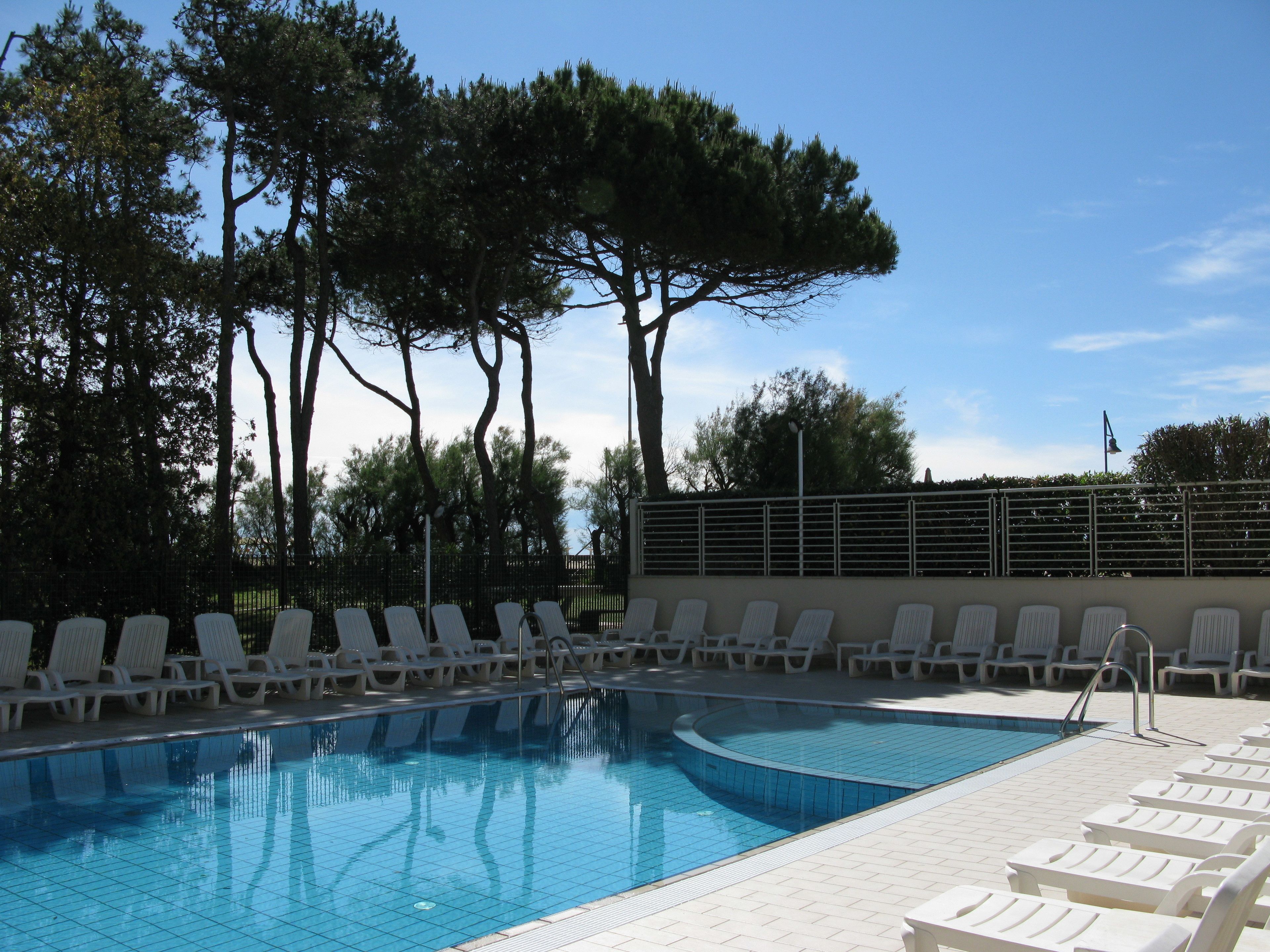 A swimming pool with white lounge chairs and trees in the background.