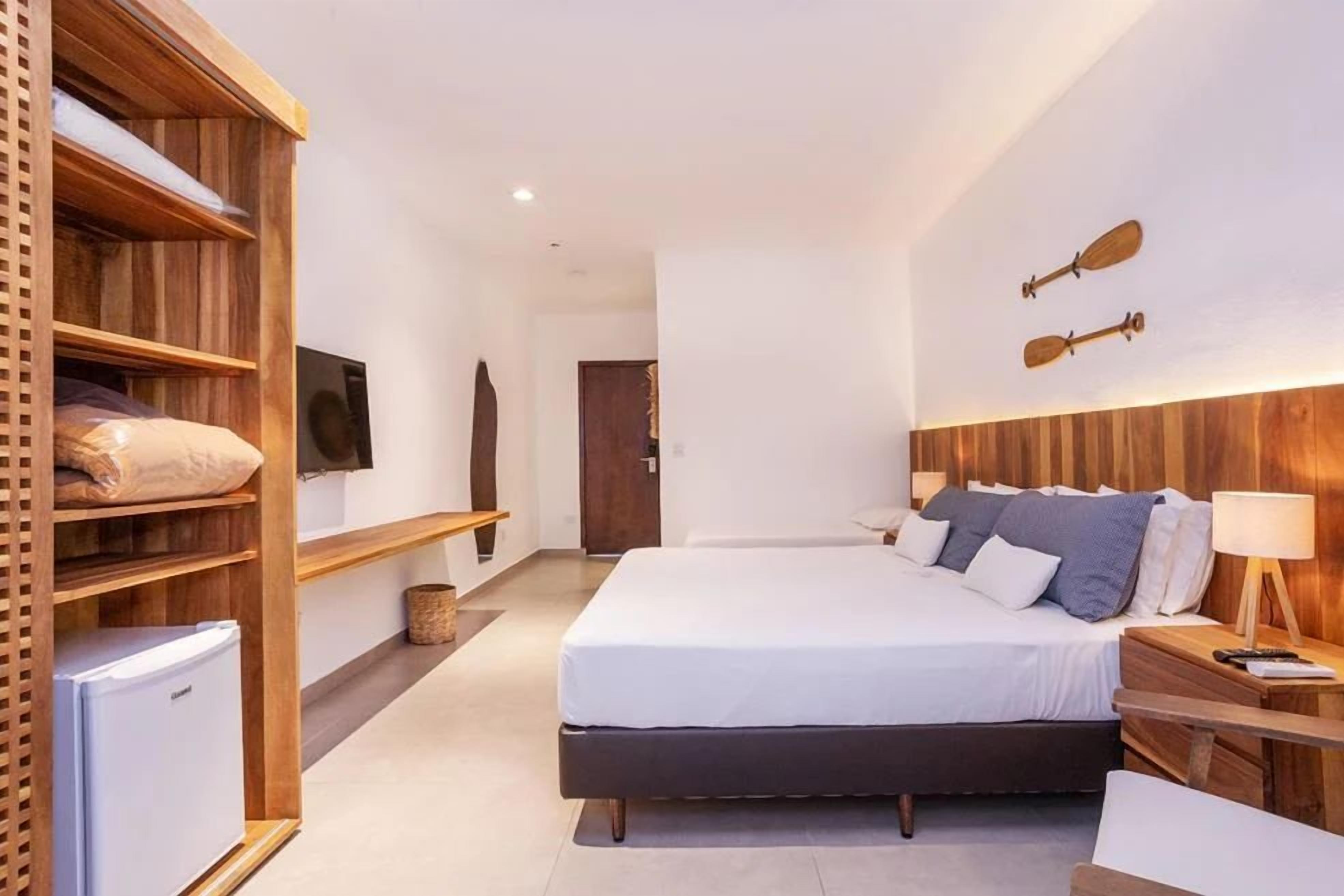 A modern hotel room with a large bed, wooden shelving, a television, and a small refrigerator.