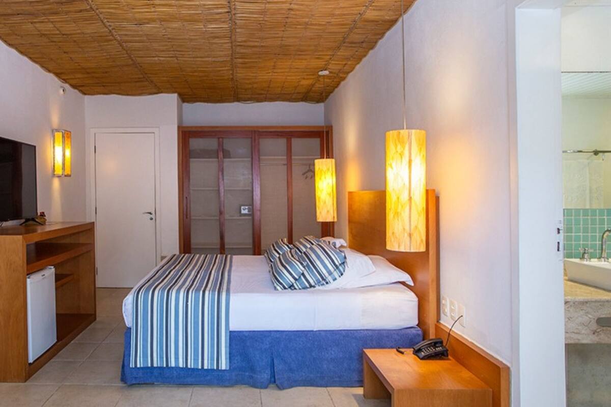 A hotel room with a bed, bedside lamps, a TV, a desk, and a small fridge.