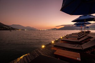 Um deck de madeira com cadeiras de descanso e guarda-sóis, com vista para um corpo d'água calmo ao entardecer.