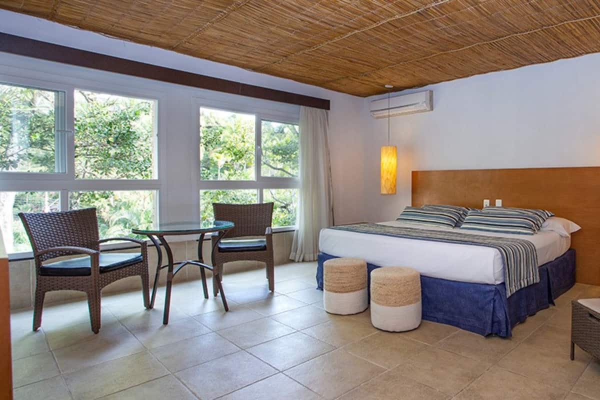 Habitación de hotel con cama, dos sillas, una mesa y un ventanal grande.