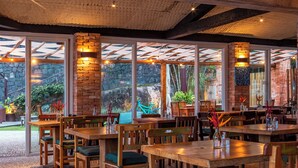 A restaurant with wooden tables and chairs, large windows, and a brick wall. - Hotel Mercedes (Ilhabela)