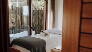 A bedroom with a bed, a wooden bench, a small table, and a view of a balcony with a wooden fence. - Hotel Mercedes (Ilhabela)