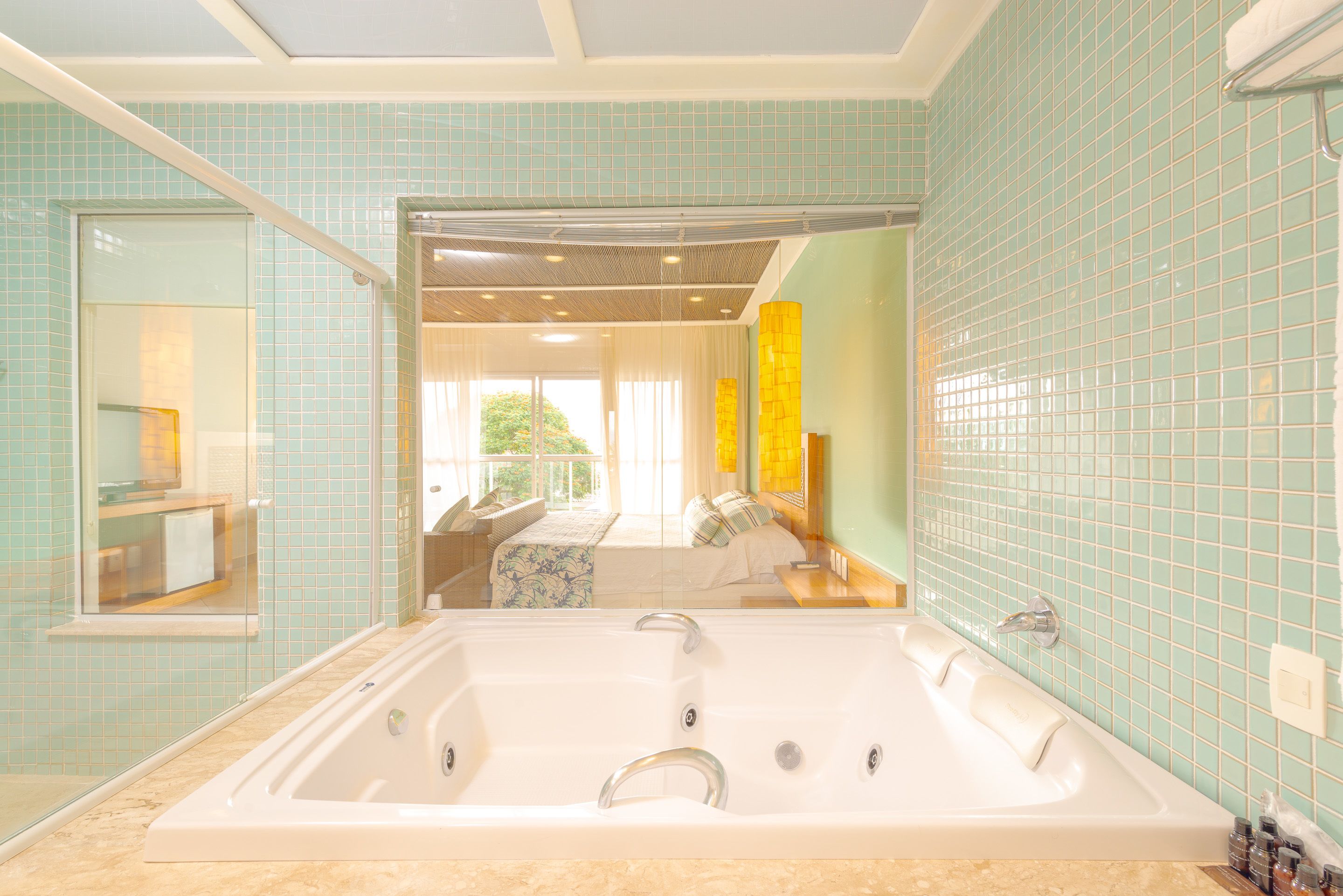 Un bagno con una grande vasca, un box doccia in vetro e vista su una camera da letto con un letto e una finestra.