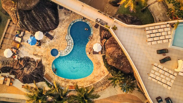 An aerial view of a resort with a swimming pool, lounge areas, and a thatched-roof structure. - Hotel Mercedes (Ilhabela)