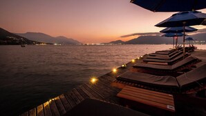 A wooden deck with lounge chairs and umbrellas, overlooking a calm body of water at dusk. - Hotel Mercedes (Ilhabela)