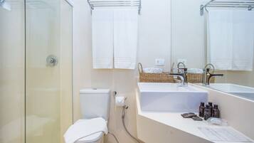 Een moderne badkamer met een douchecabine van glas, een toilet, een wastafel met spiegel en een handdoekhouder.