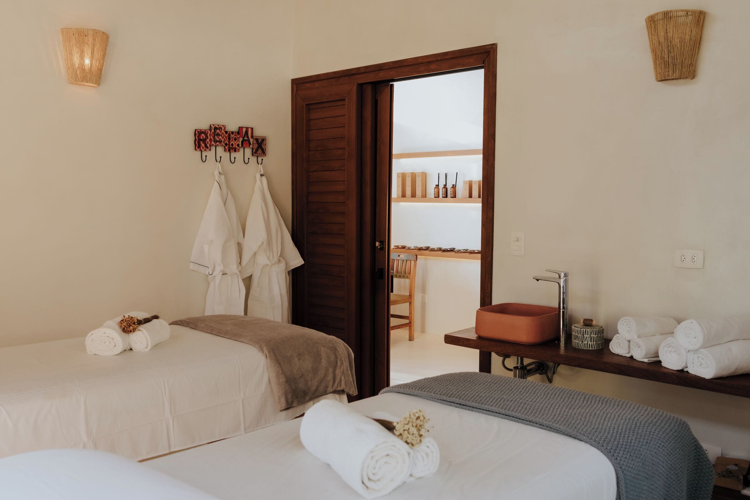 A hotel room with two beds, a bathroom with a sink and mirror, and a door leading to a balcony with a view.