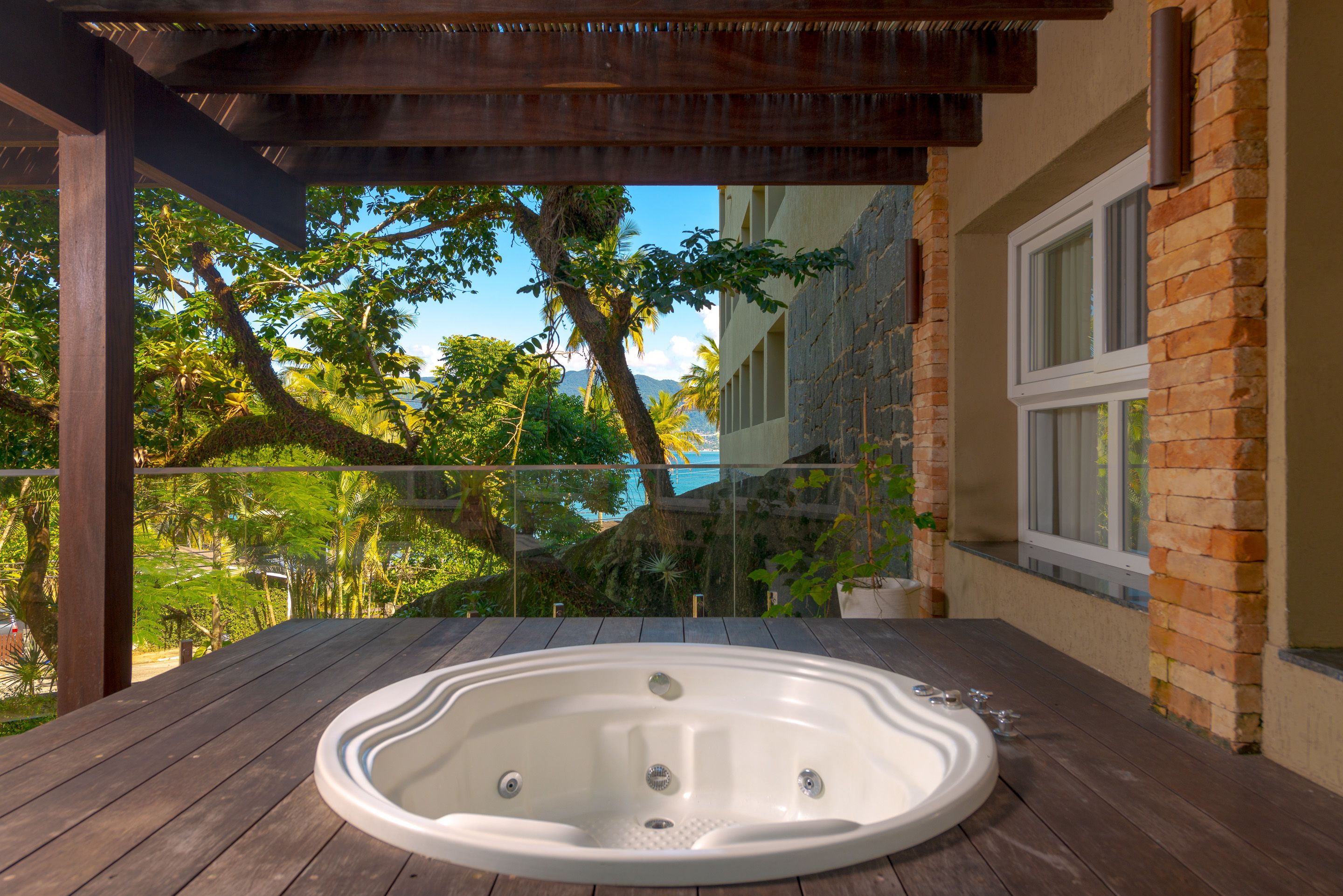 A wooden deck with a hot tub, overlooking a lush garden and a body of water.