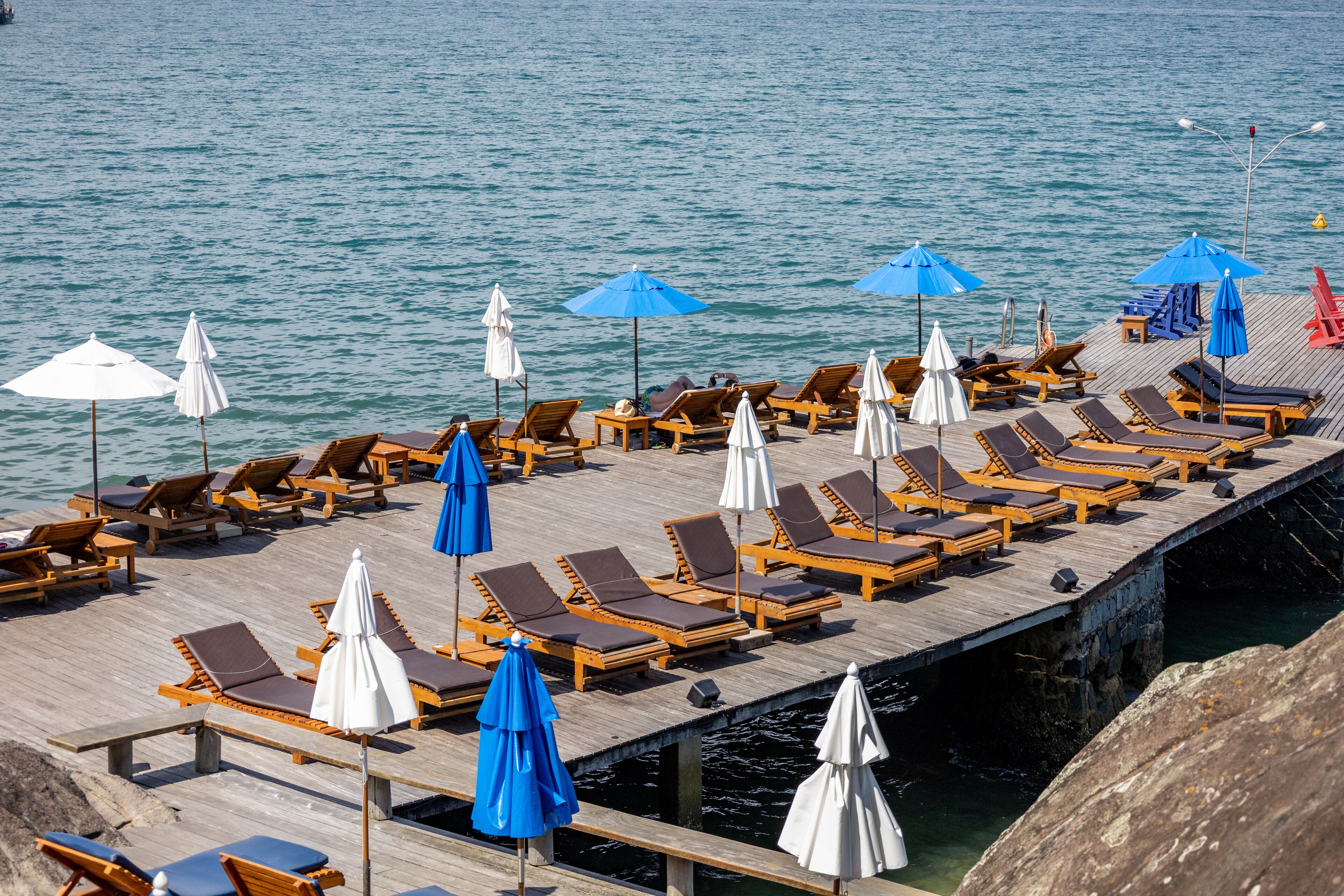 A wooden pier with rows of sun loungers and umbrellas, overlooking calm water.
