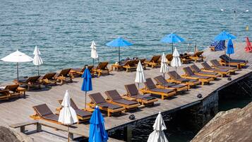 A wooden pier with rows of sun loungers and umbrellas, overlooking calm water.