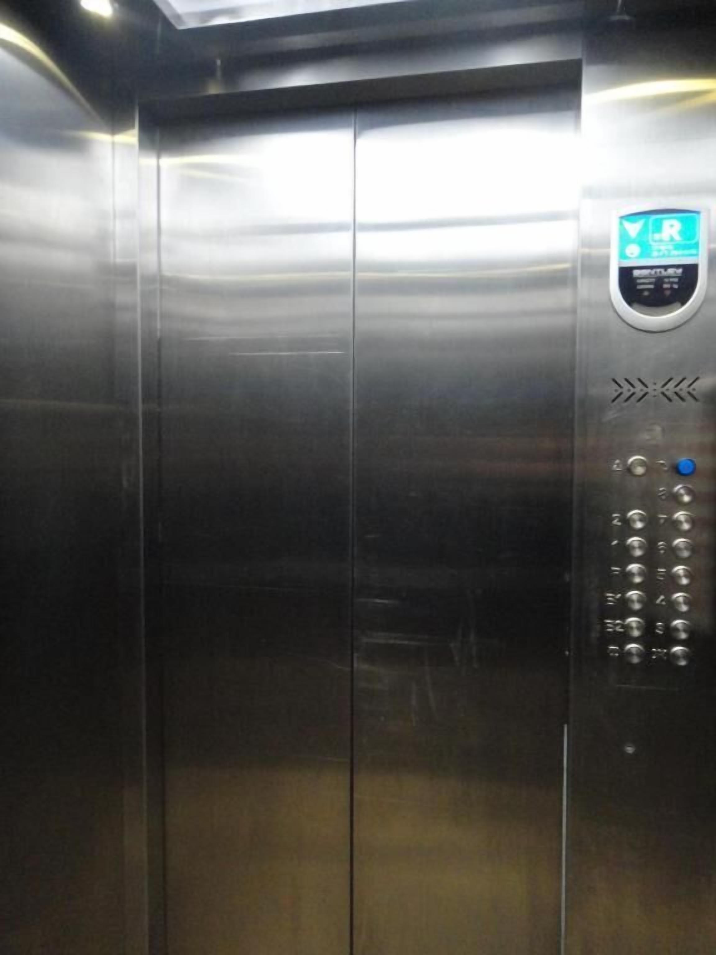 Un ascenseur aux parois métalliques, doté d’un panneau de commande avec une flèche indiquant la direction et un bouton.