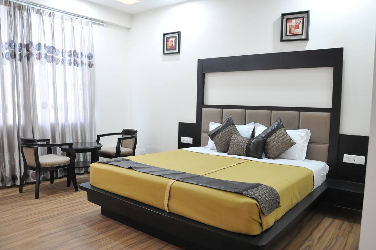 Una habitación de hotel con una cama grande, una mesita pequeña, dos sillas y una ventana con cortinas.