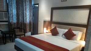 Ein Hotelzimmer mit einem großen Bett, einem Nachttisch, einem Sessel und einem Fenster mit Vorhängen.