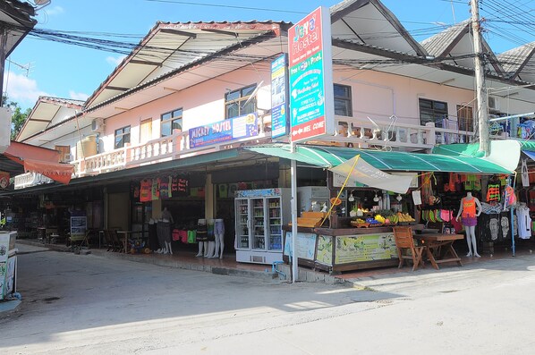 A hostel with a signboard advertising free pool access, a small shop with a fruit stand, and a mannequin display outside. - Mickey Hostel (Ko Pha-ngan)