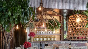 A restaurant with a rustic wooden bar, white chairs, and a hanging light fixture.