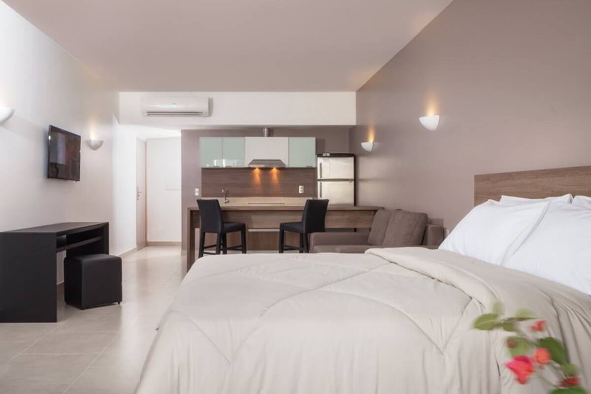 A modern hotel room with a large bed, a desk, and a kitchenette area.