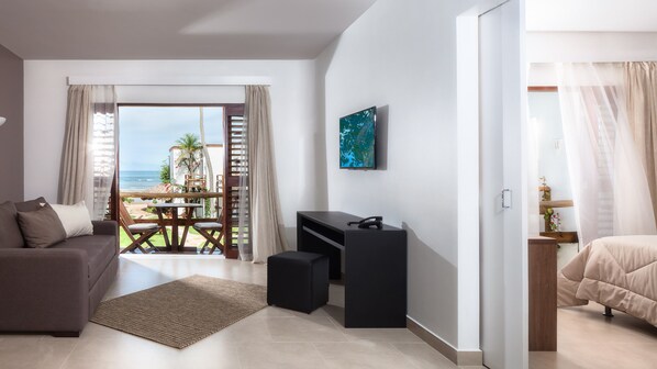 A modern hotel room with a sofa, a desk, a bed, and a view of the ocean.