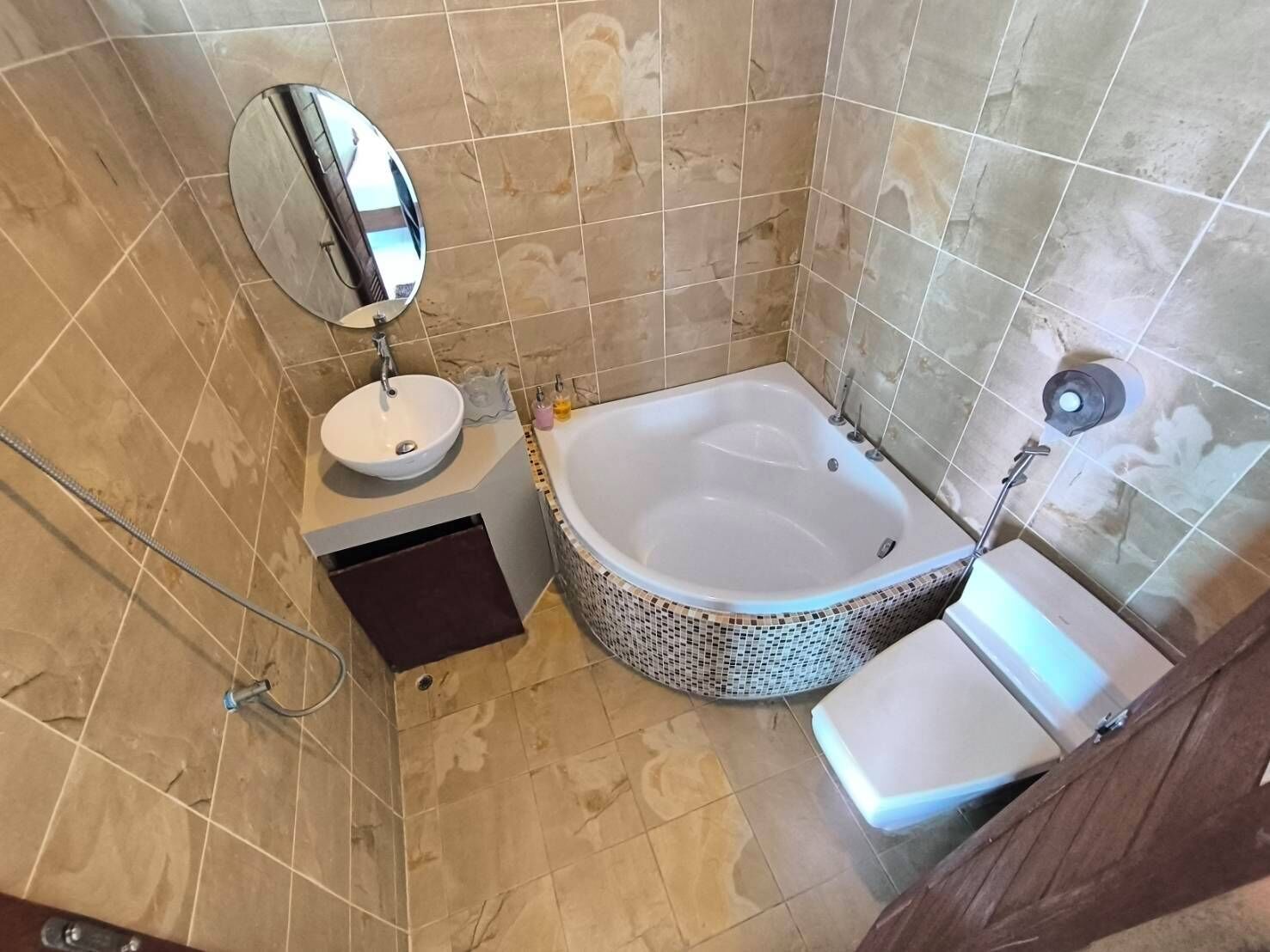 Un baño con una bañera independiente, un espejo redondo, un lavamanos y un inodoro.