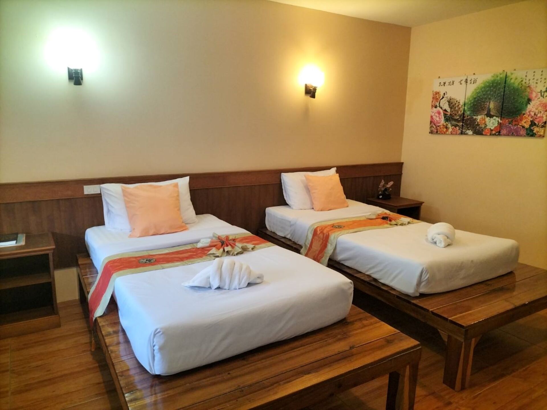 A hotel room with two single beds, wooden headboards, a wooden bench, and a wall-mounted light fixture.