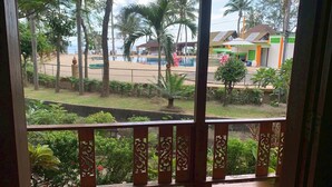 Une vue depuis un balcon donnant sur une piscine, des palmiers et une plage en arrière-plan.