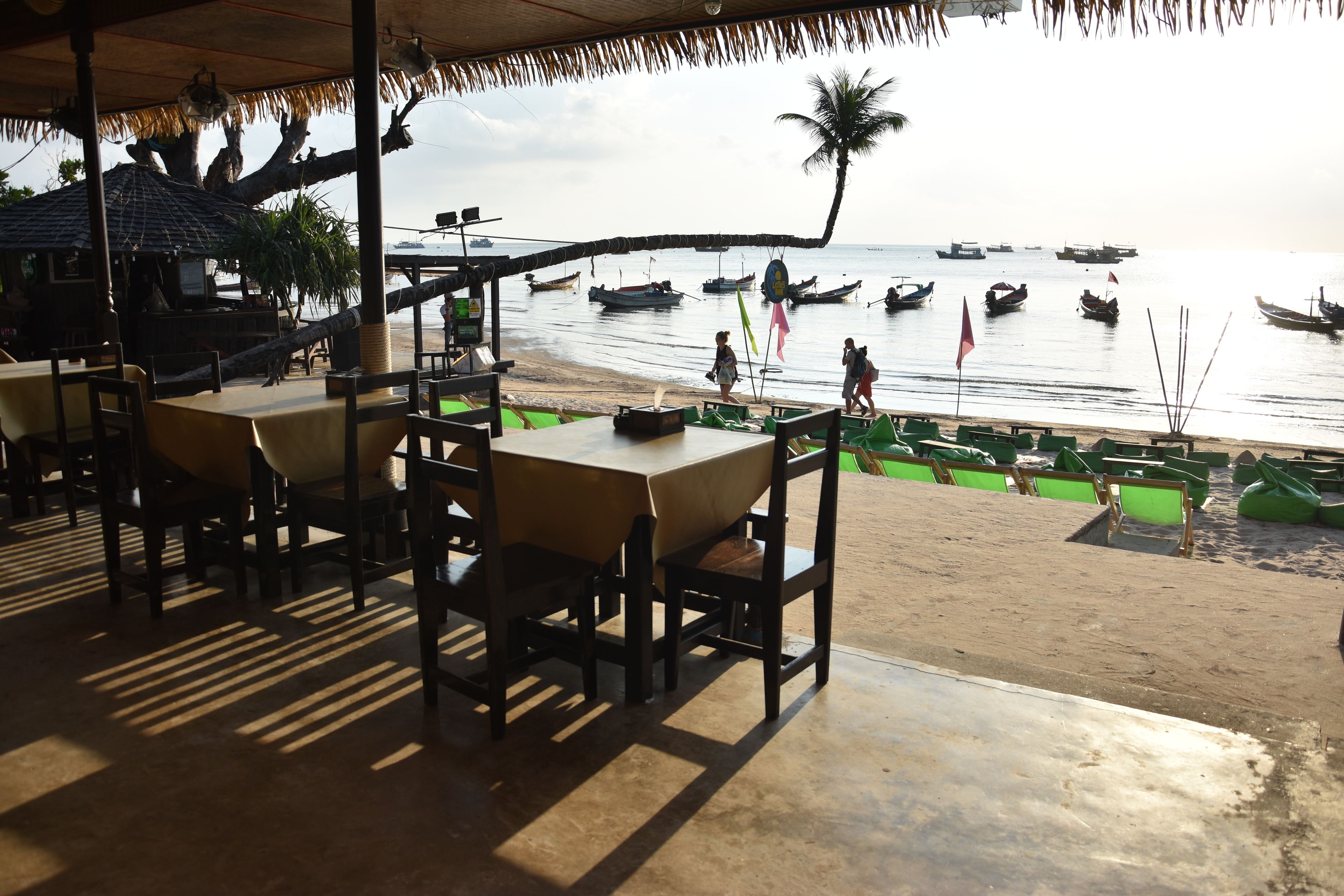 Un restaurante frente al mar con mesas y sillas, con vistas al océano y varios barcos.