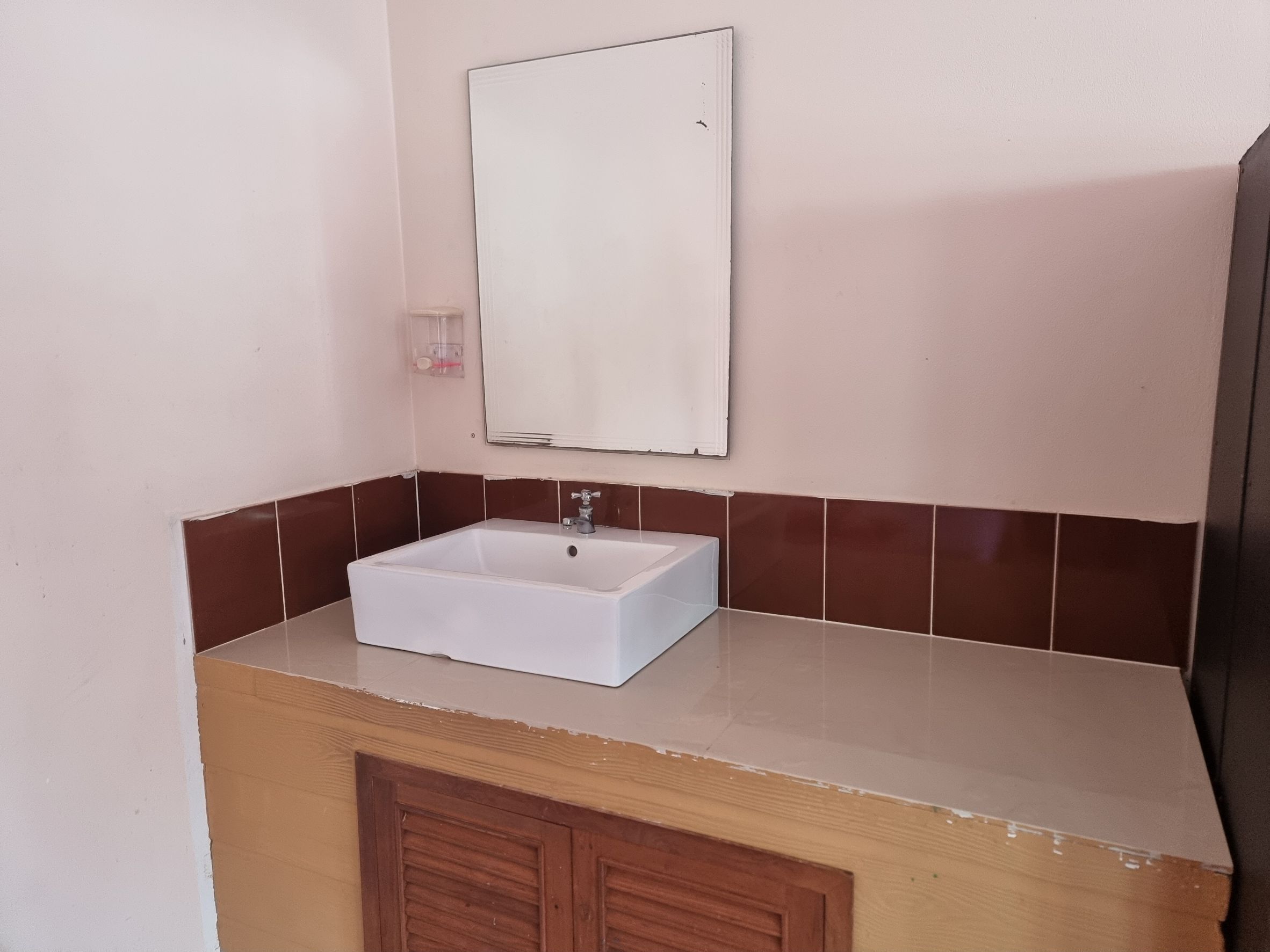 A bathroom with a white sink, brown tiles, and a mirror above it.