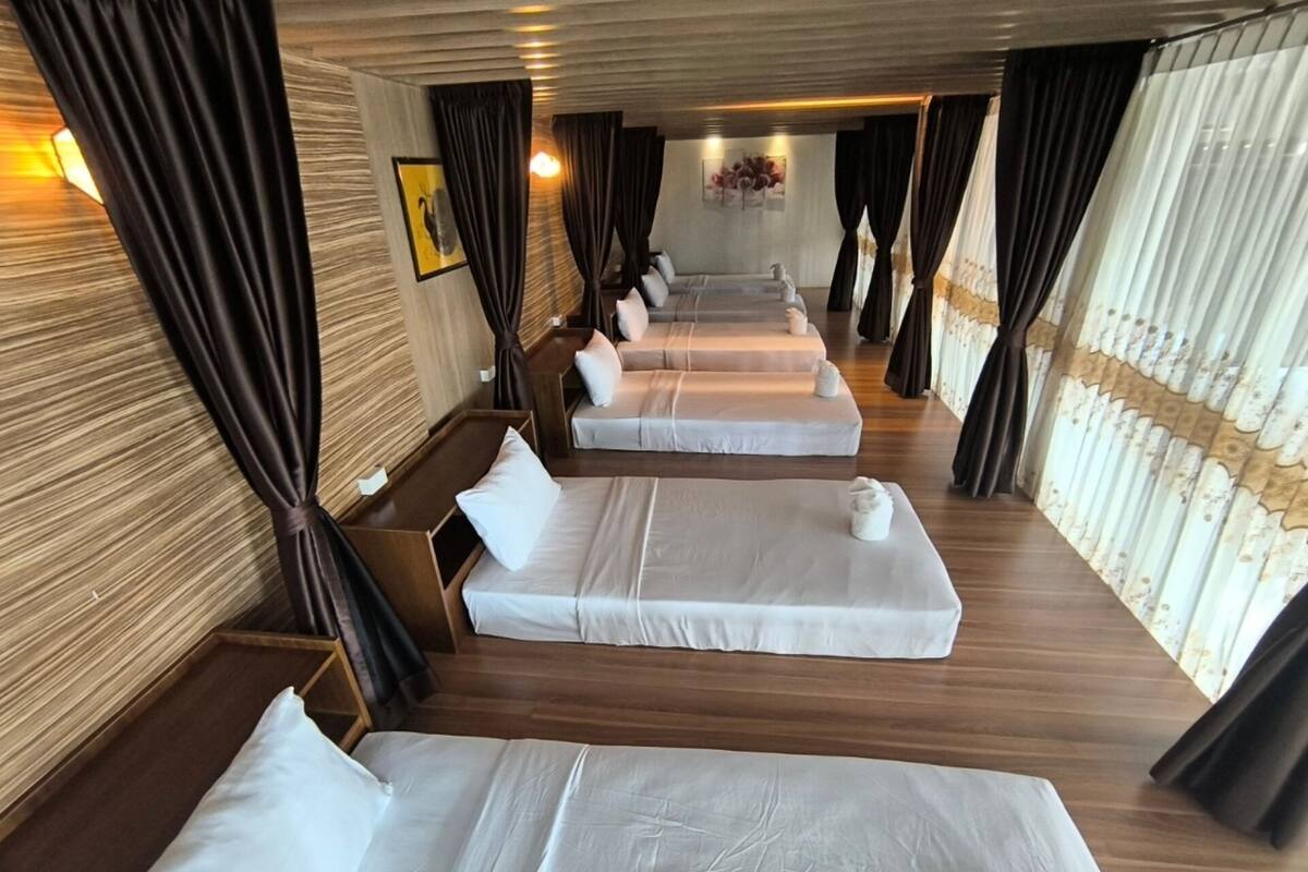 Een hotelkamer met houten vloeren, meerdere bedden op rij en donkere gordijnen.