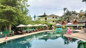 Une piscine entourée de chaises longues et de parasols, elle-même bordée de verdure et d’un bâtiment doté d’un toit végétalisé.