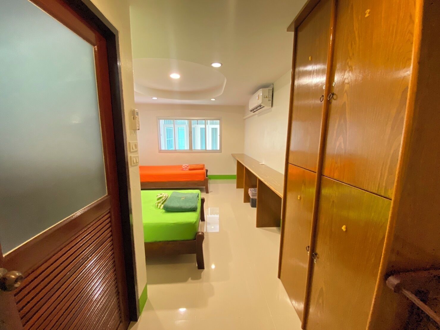 A room with two beds, a wooden wardrobe, a window, and a ceiling light.