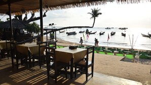 Un restaurant situé en bord de mer, avec des tables et des chaises, offrant une vue sur la mer et sur plusieurs bateaux.