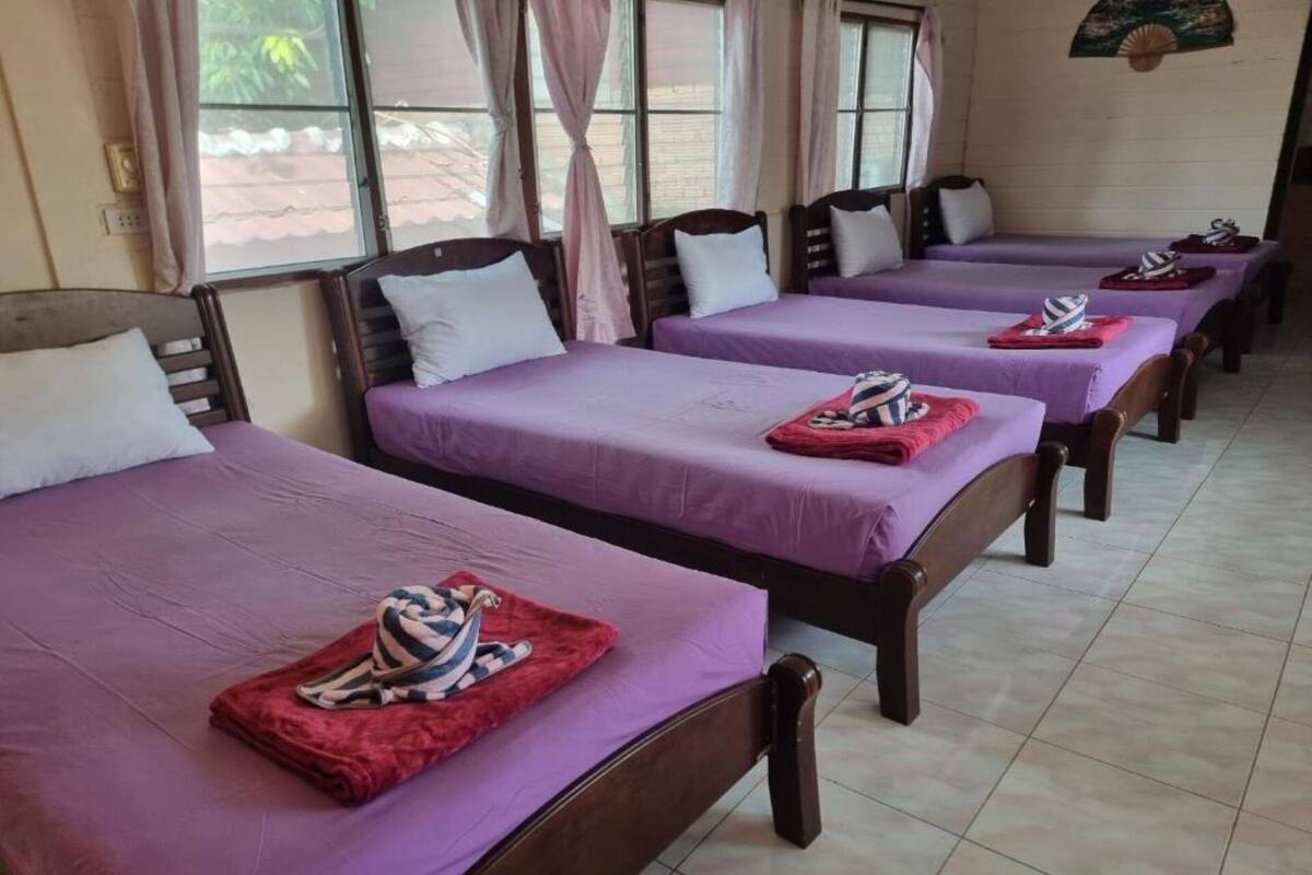 Een hotelkamer met vier enkele bedden, elk met een paarse dekbedovertrek en een rode handdoek.