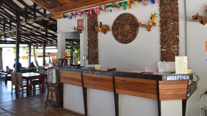 A reception desk with a 'RECEPTION' sign, surrounded by wooden carvings and flags. - JP Resort Koh Tao (Koh Tao)