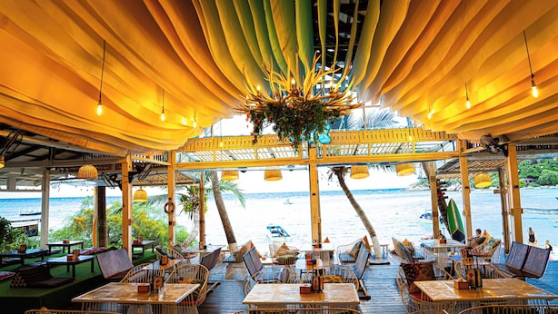 An outdoor dining area with tables and chairs, overlooking a body of water with boats. - JP Resort Koh Tao (Koh Tao)